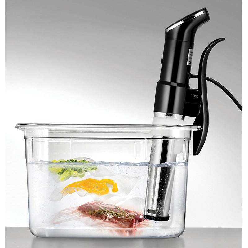 Unold Sous Vide Stick Time met klem aan een transparante bak water met drie gevacumeerde zakken groente, fruit en vlees