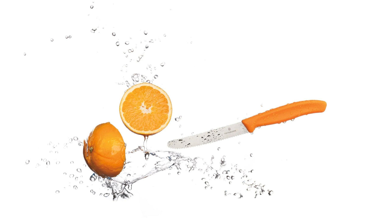 Oranje tomatenmes naast een doorgesneden sinaasappel met opspattend water