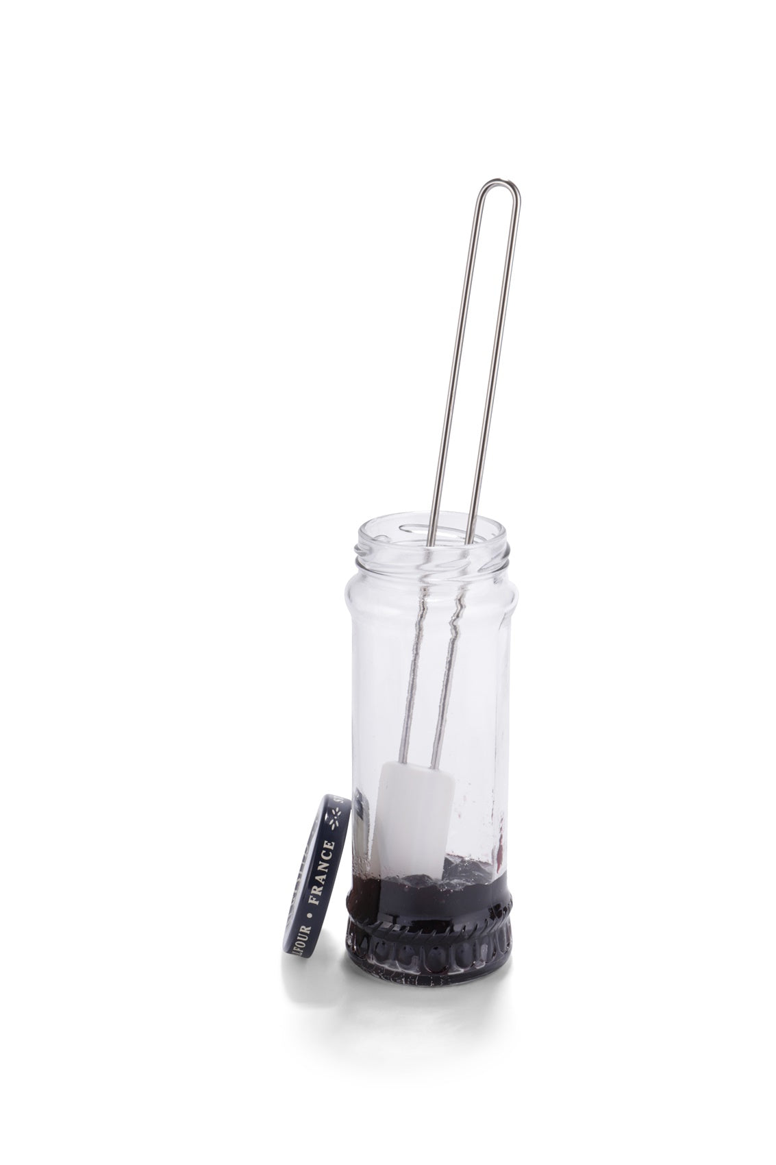 Schraper met wit blad in een hoog glas waar nog een restant donkere jam op de bodem zit, de lussteel steekt boven de rand uit