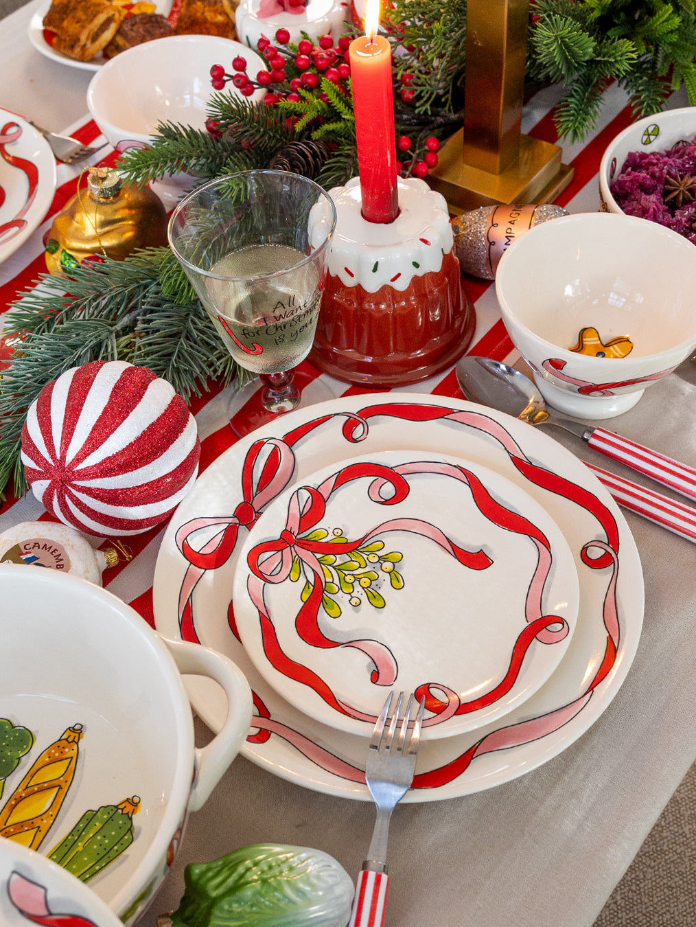 Het gebaksbord met maretak en lint op een gedekte kersttafel met rode kaars en dennentakken
