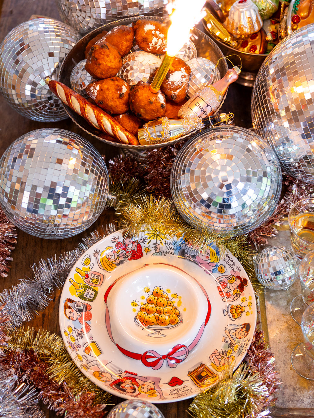 De borrelschaal tussen discoballen, klatergoud en oliebollen op een houten tafel