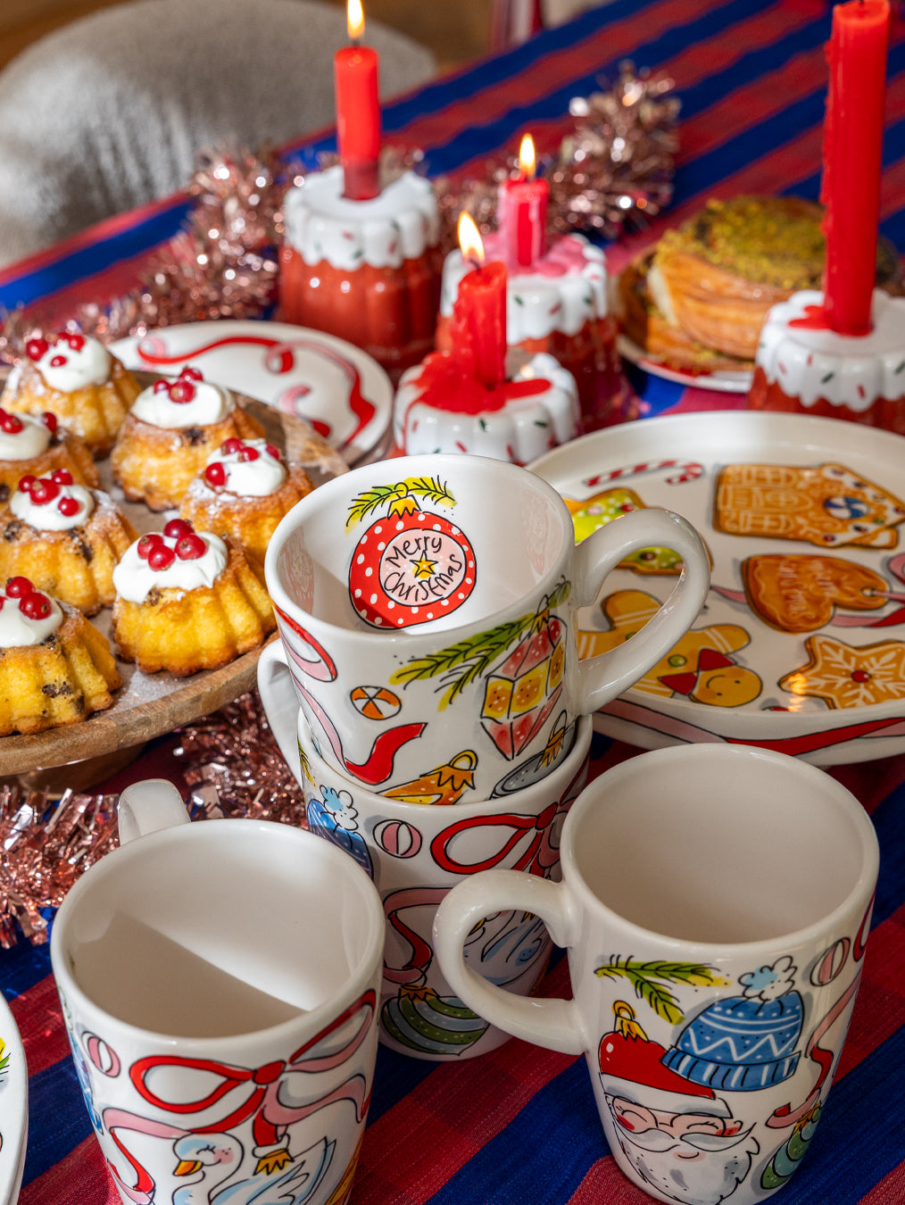 Kersttafel met rode kaarsen, klatergoud en mokken met kerstballen