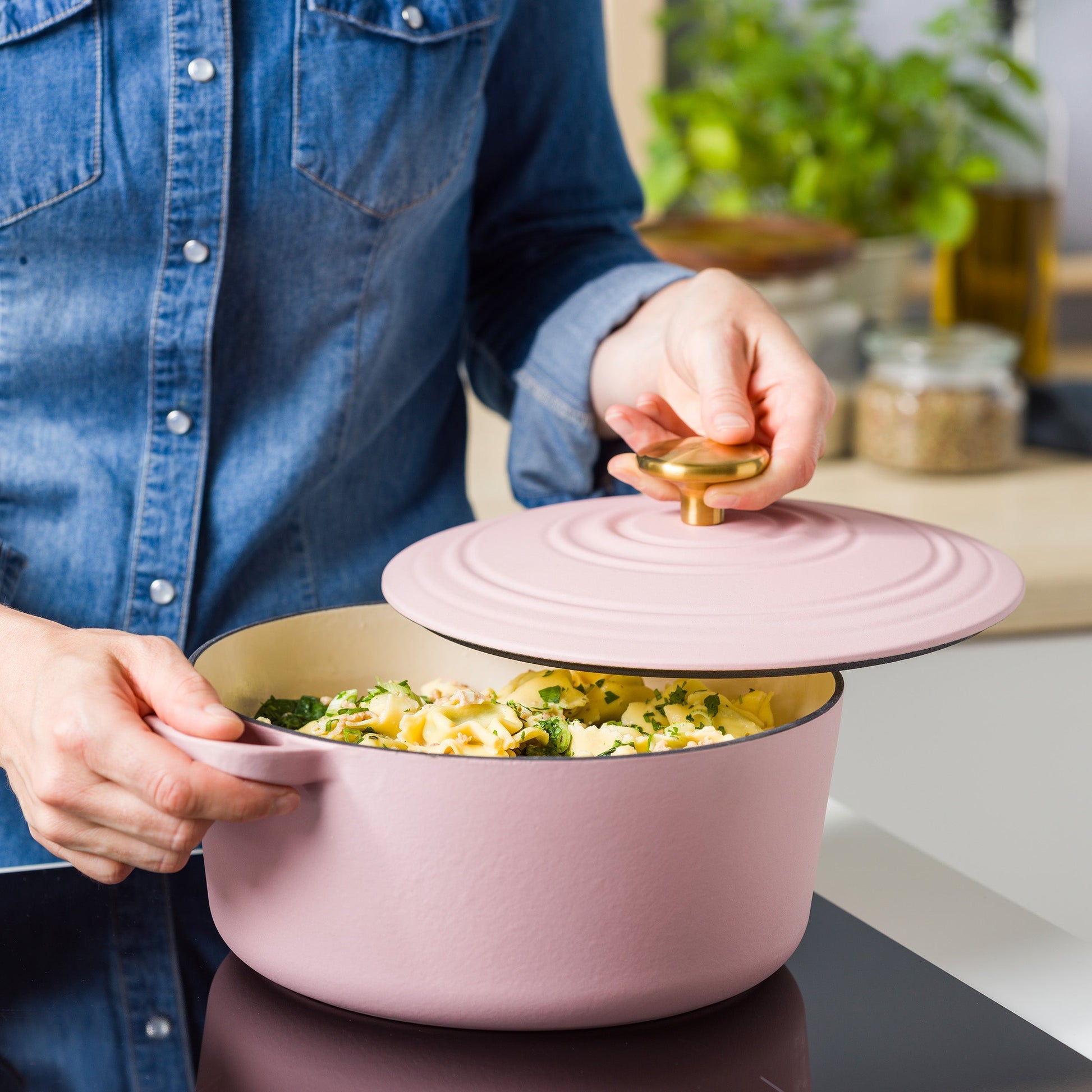 Persoon tilt de roze deksel met goudkleurige knop van de BK braadpan met pasta