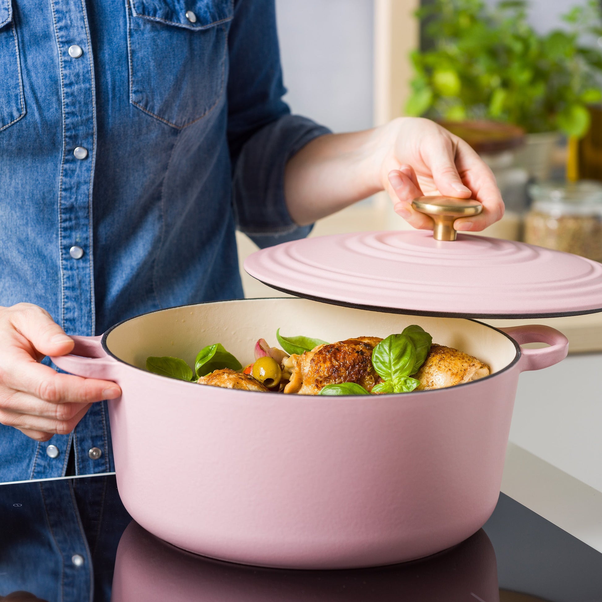 Persoon tilt de roze deksel van de BK braadpan met kip, basilicum en olijven