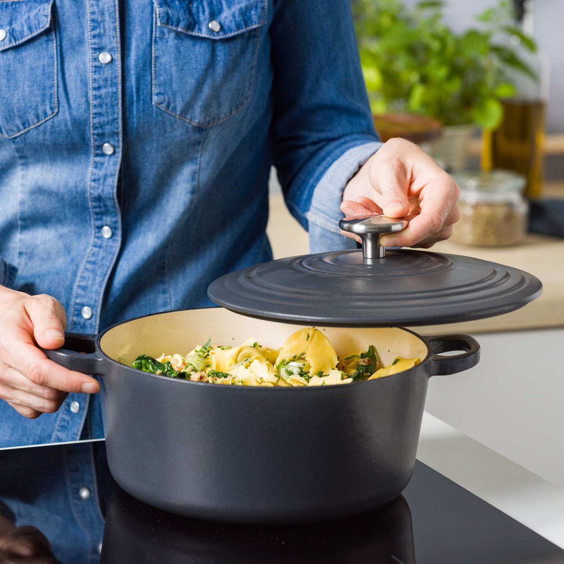 Persoon tilt de antracietgrijze deksel van de BK braadpan met tortellini en spinazie