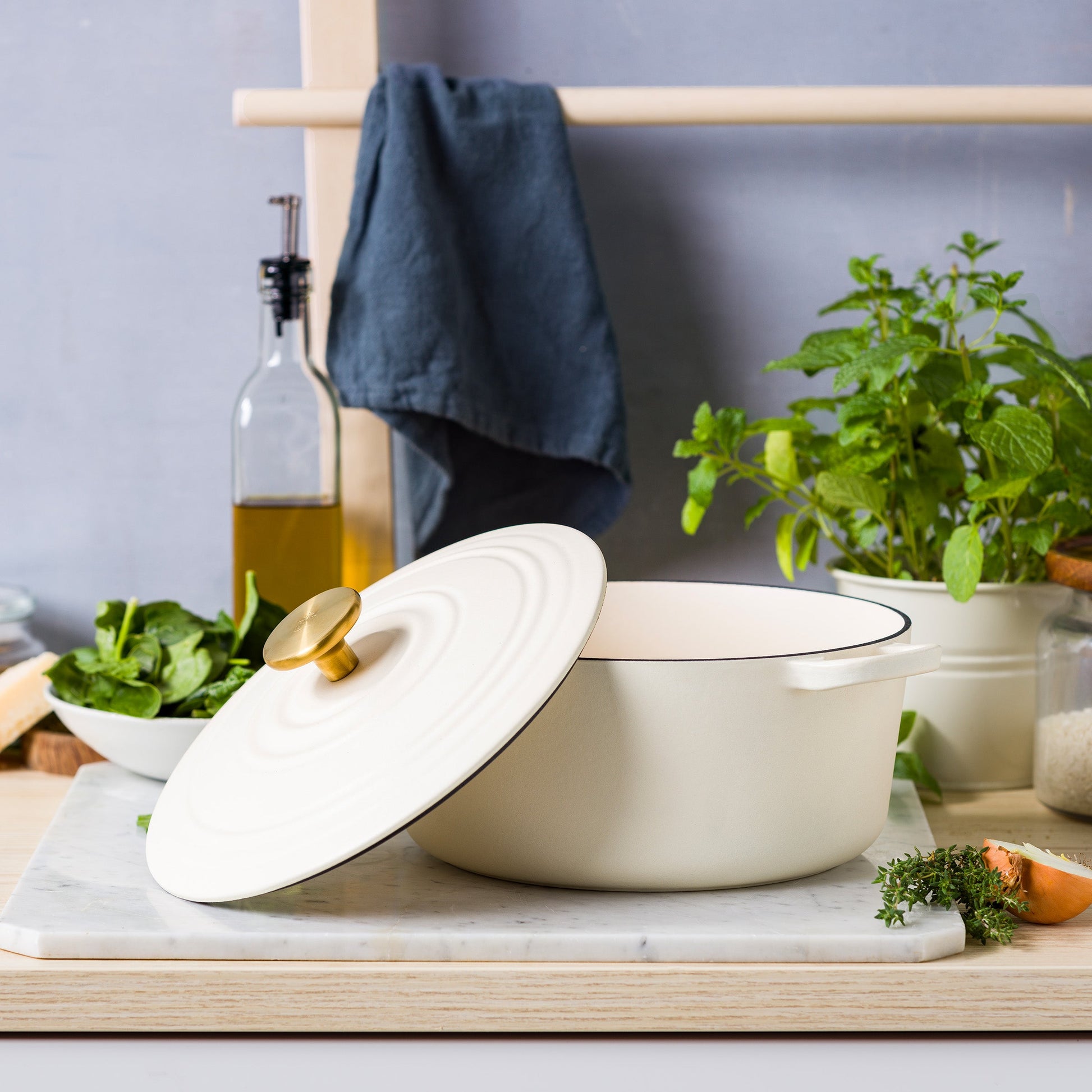 Crèmewitte BK Bourgogne braadpan met schuin geplaatste deksel op marmer, spinazie en tijm ernaast