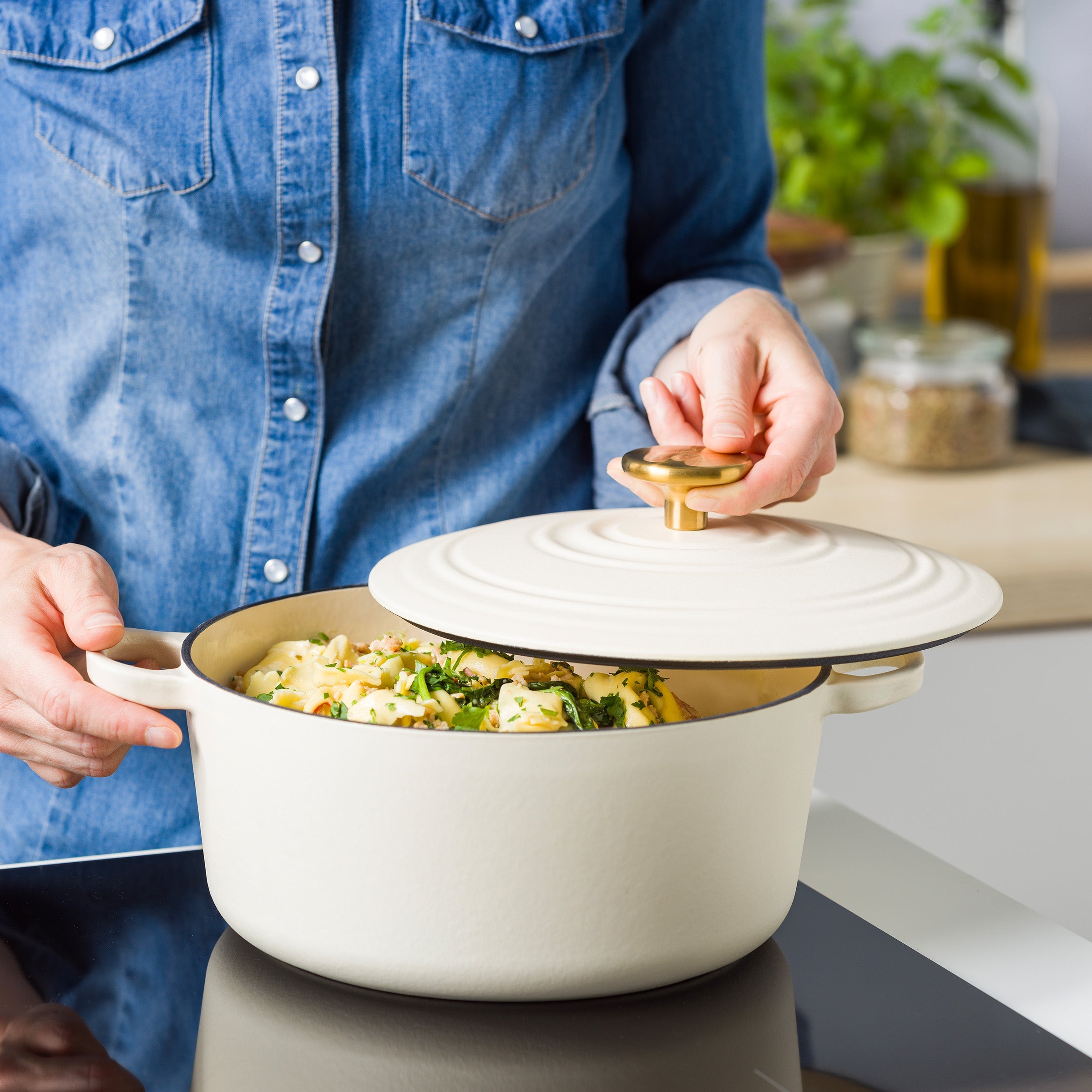 Persoon tilt de crèmewitte deksel met goudkleurige knop van de BK braadpan met pasta