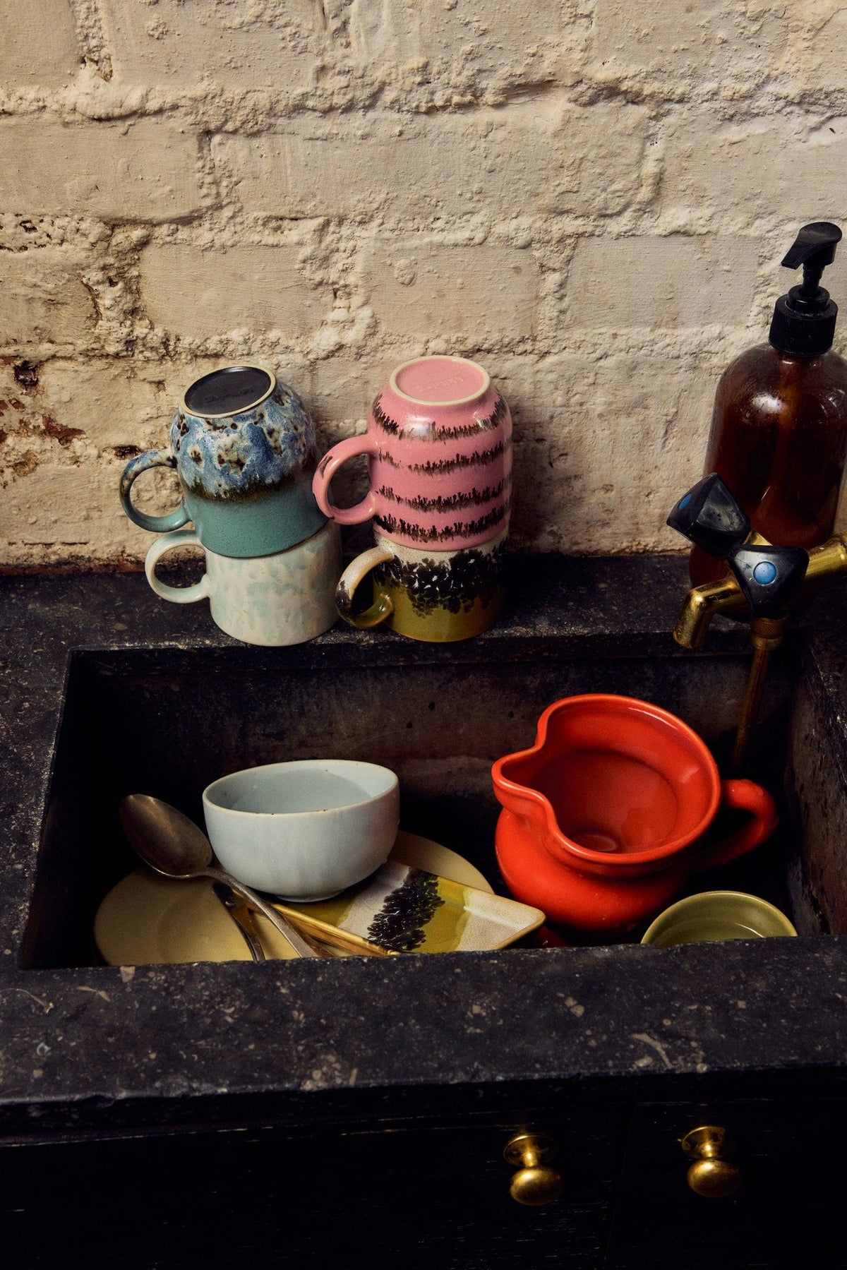 Chef Ceramics kom Soft Blue in een stenen gootsteen naast een rode kan en omgekeerde mokken tegen een witte bakstenen muur