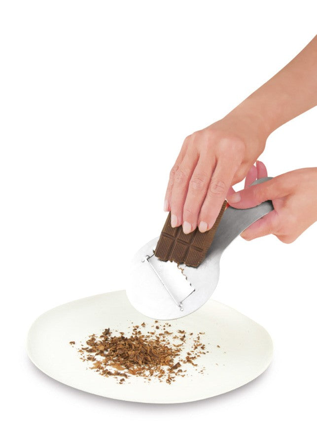 Ibili Truffel-/Chocoladeschaaf in gebruik, hand schaaft chocoladekrullen van een reep boven een bord