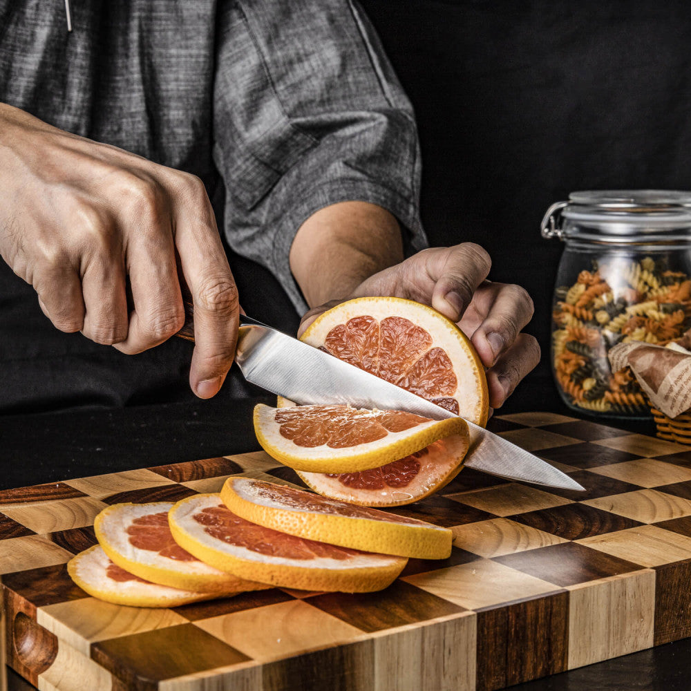 Handen snijden met het Kazoku Nisei fileermes een grapefruit in plakken op een snijplank met ruitpatroon
