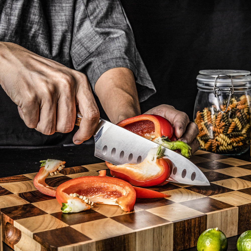 Handen snijden met de Kazoku Nisei santoku een rode paprika op een snijplank met ruitpatroon
