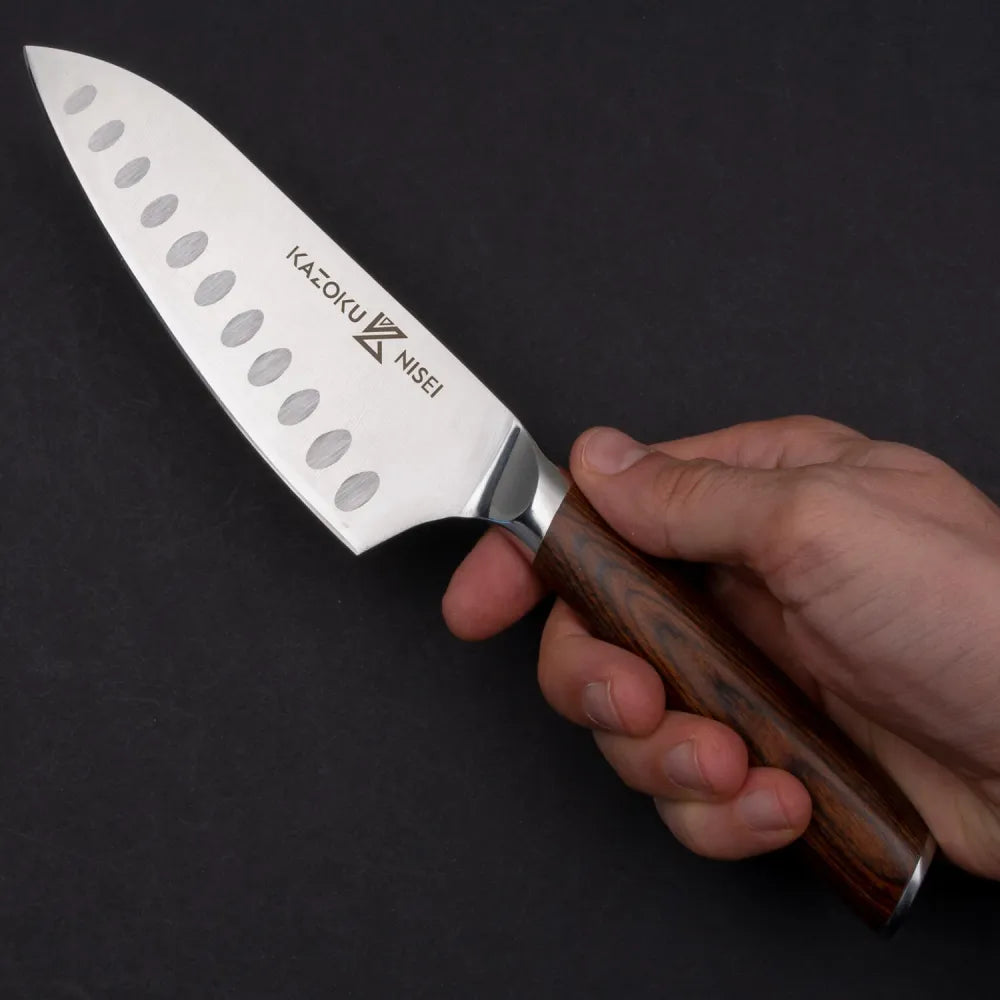 Hand houdt de Kazoku Nisei santoku vast tegen een donkere achtergrond