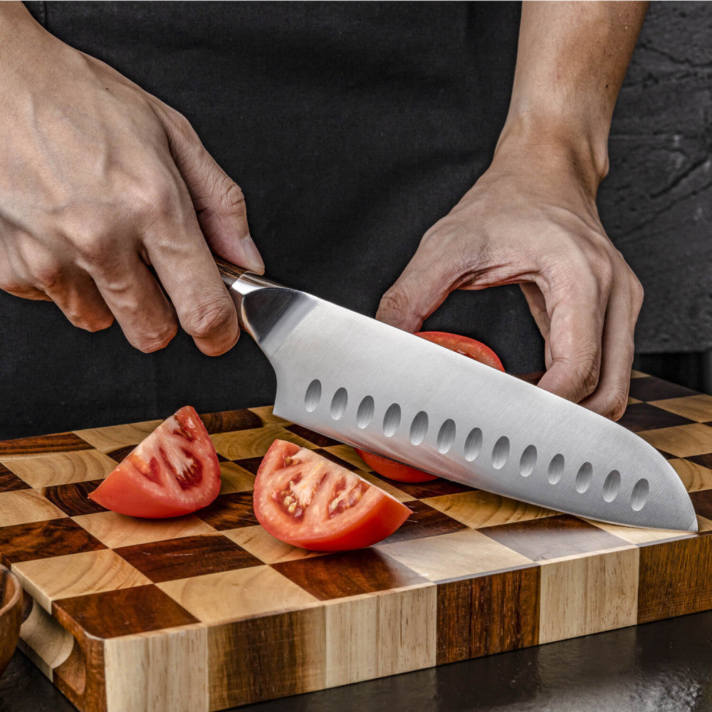 Handen snijden met de Kazoku Nisei santoku 18 cm een tomaat op een snijplank met ruitpatroon