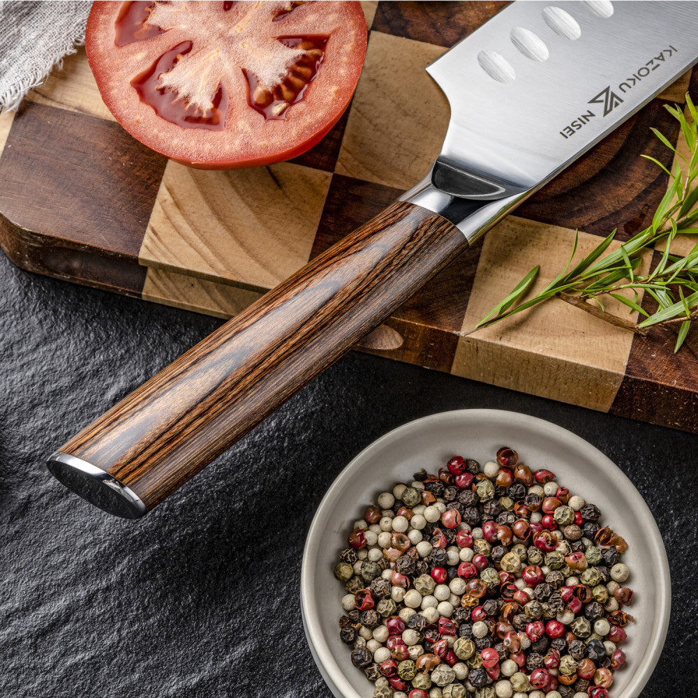 Close-up van de pakkahouten greep van de Kazoku Nisei santoku 18 cm naast een schaaltje peperkorrels