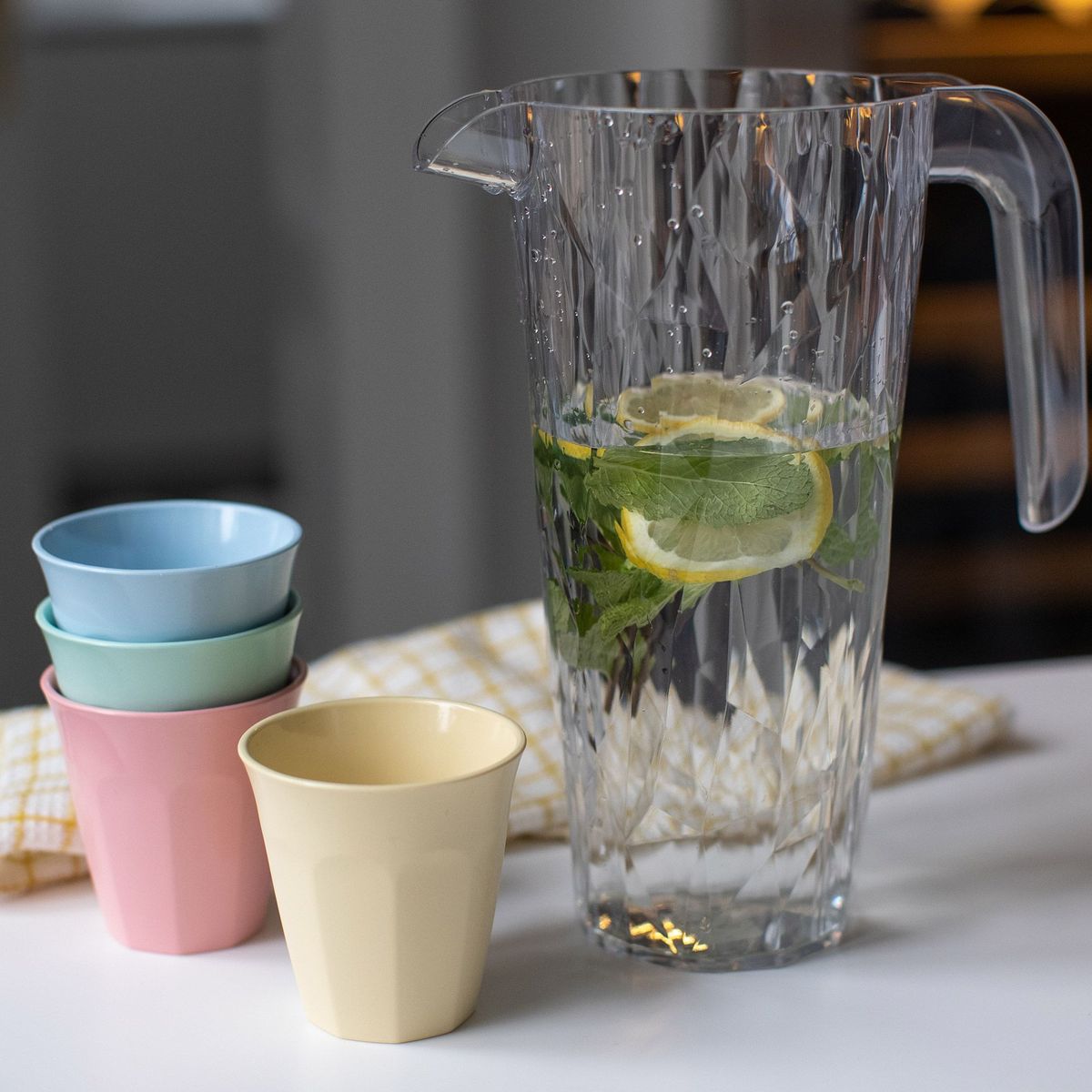 De vier pastelkleurige bekers naast een karaf water met citroen