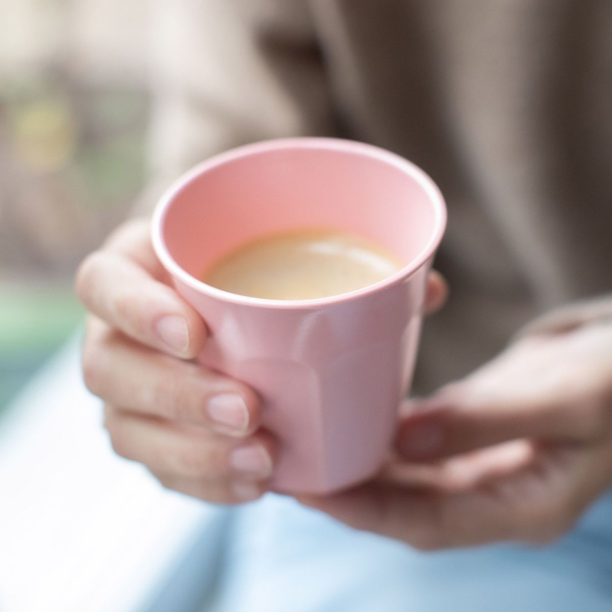 Twee handen houden de roze beker met koffie vast