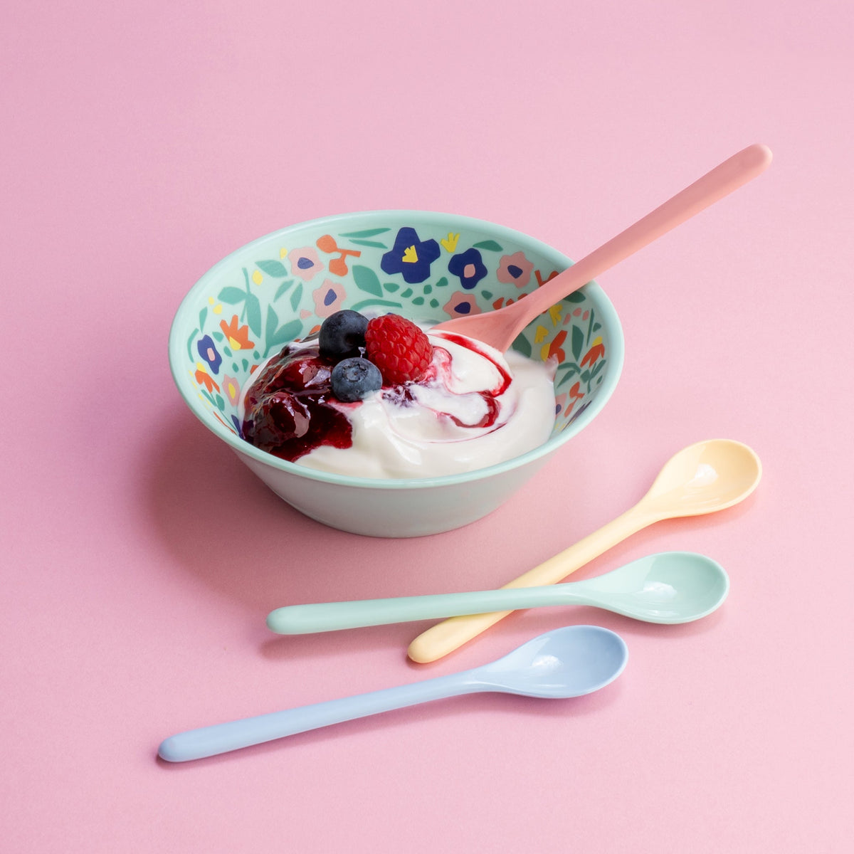 Een lepel in een kom yoghurt met bessen, de andere drie ernaast