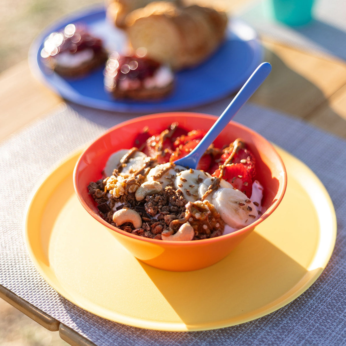 Een lange lepel in een kom granola met yoghurt op een gedekte tafel