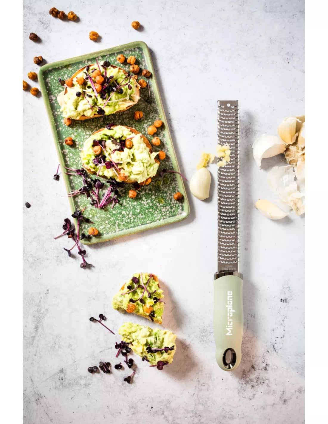 De zesteur naast twee boterhammen met avocado, met geraspte knoflook en losse teentjes ernaast