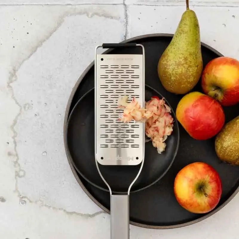 De rasp op een zwart bord met geraspte gember, naast appels en een peer
