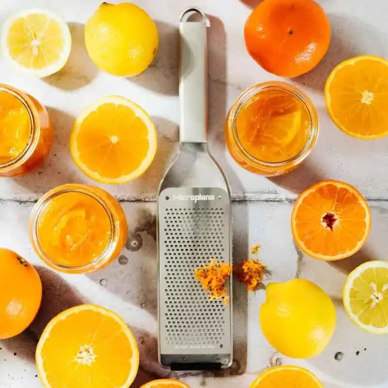 De rasp tussen gehalveerde sinaasappels en potjes marmelade, met geraspte schil op het blad