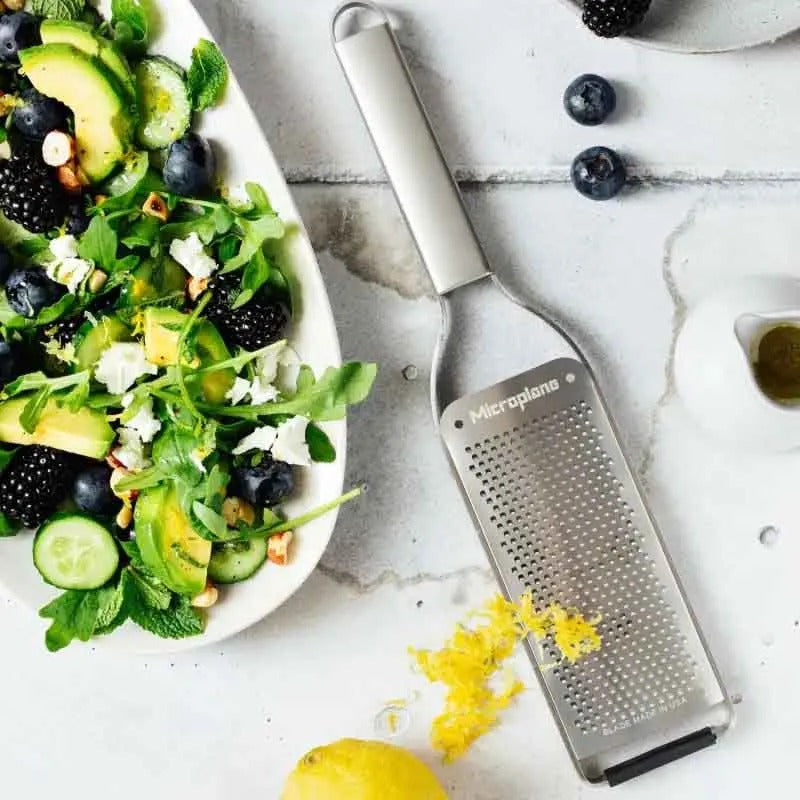 De rasp met geraspte citroenschil naast een salade met avocado en bramen