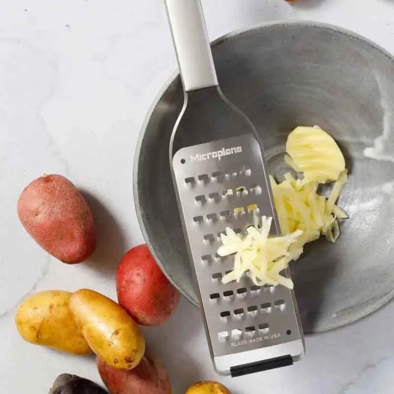 De rasp met geraspte kaas boven een grijze kom, naast rode en gele aardappels