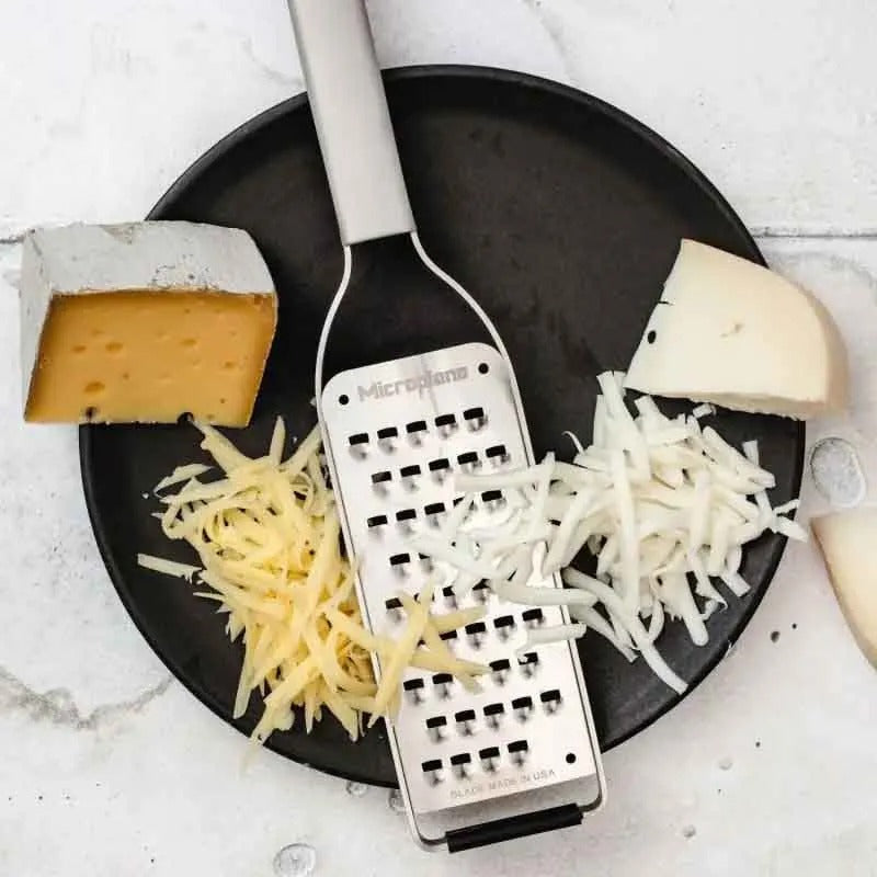 De rasp op een zwart bord met twee soorten geraspte kaas