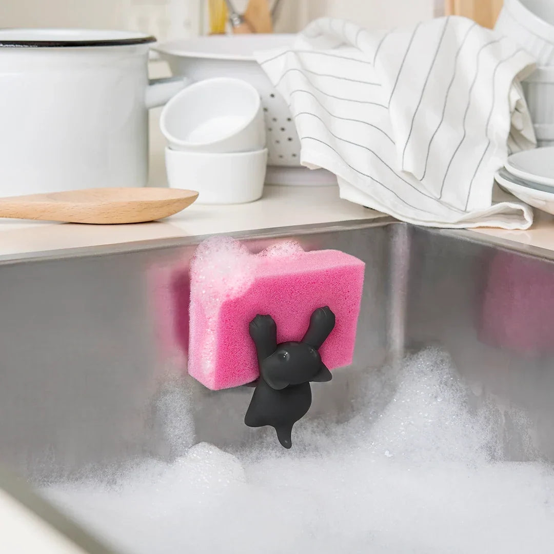 Grijze kat-sponshouder met roze spons boven een spoelbak