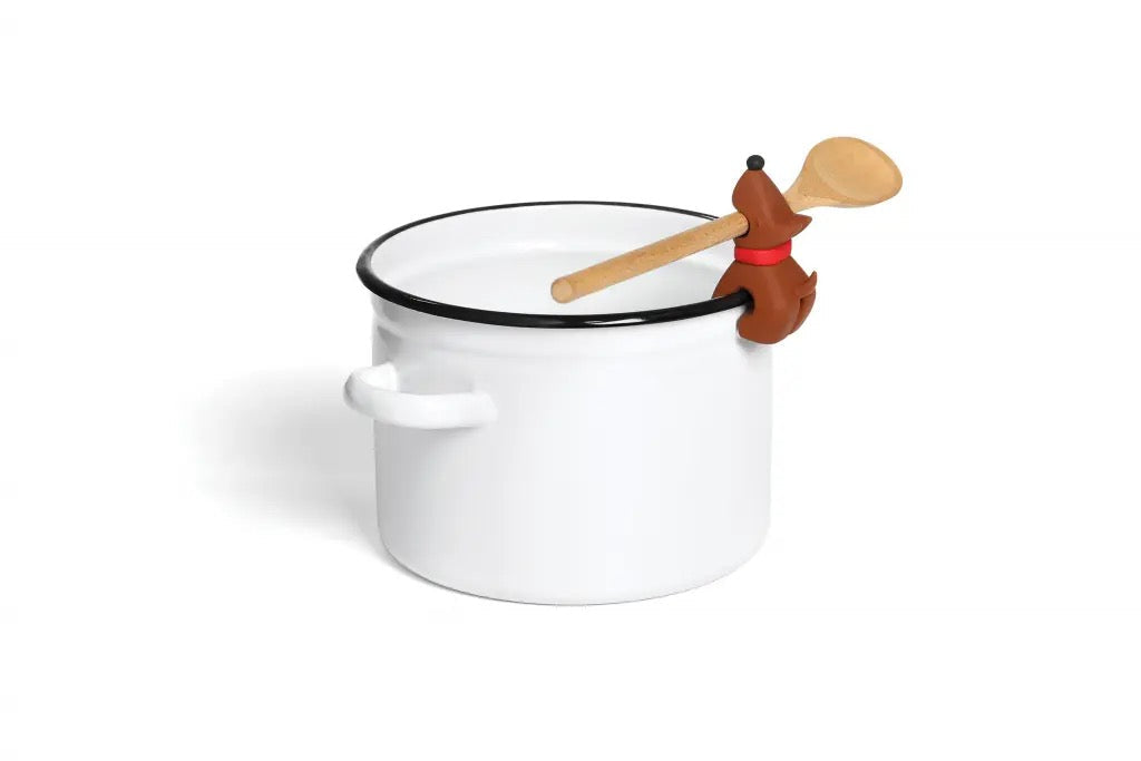 Het hondje zit op de rand van een witte pan met een lepel