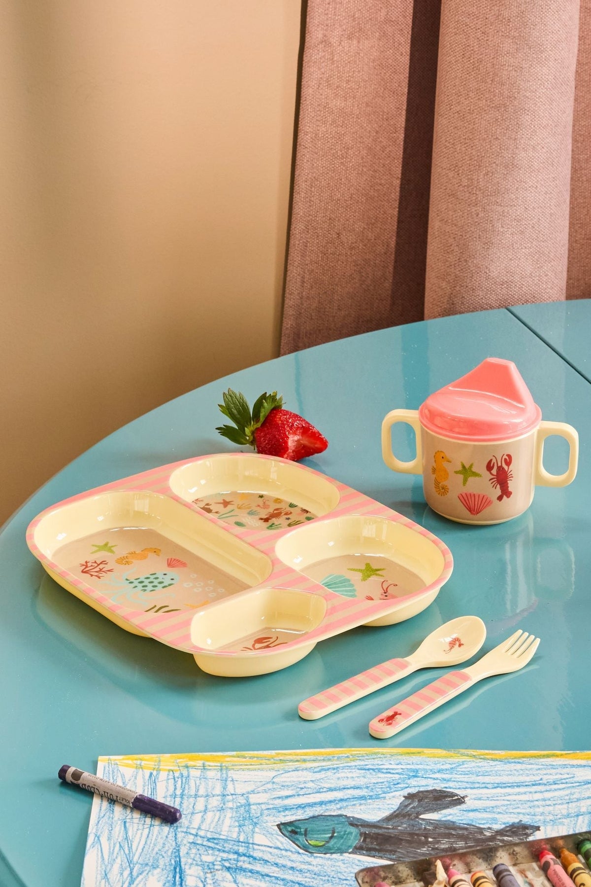 Vakjesbord met eten en tuitbeker met zeedierenprint op een blauwe kindertafel