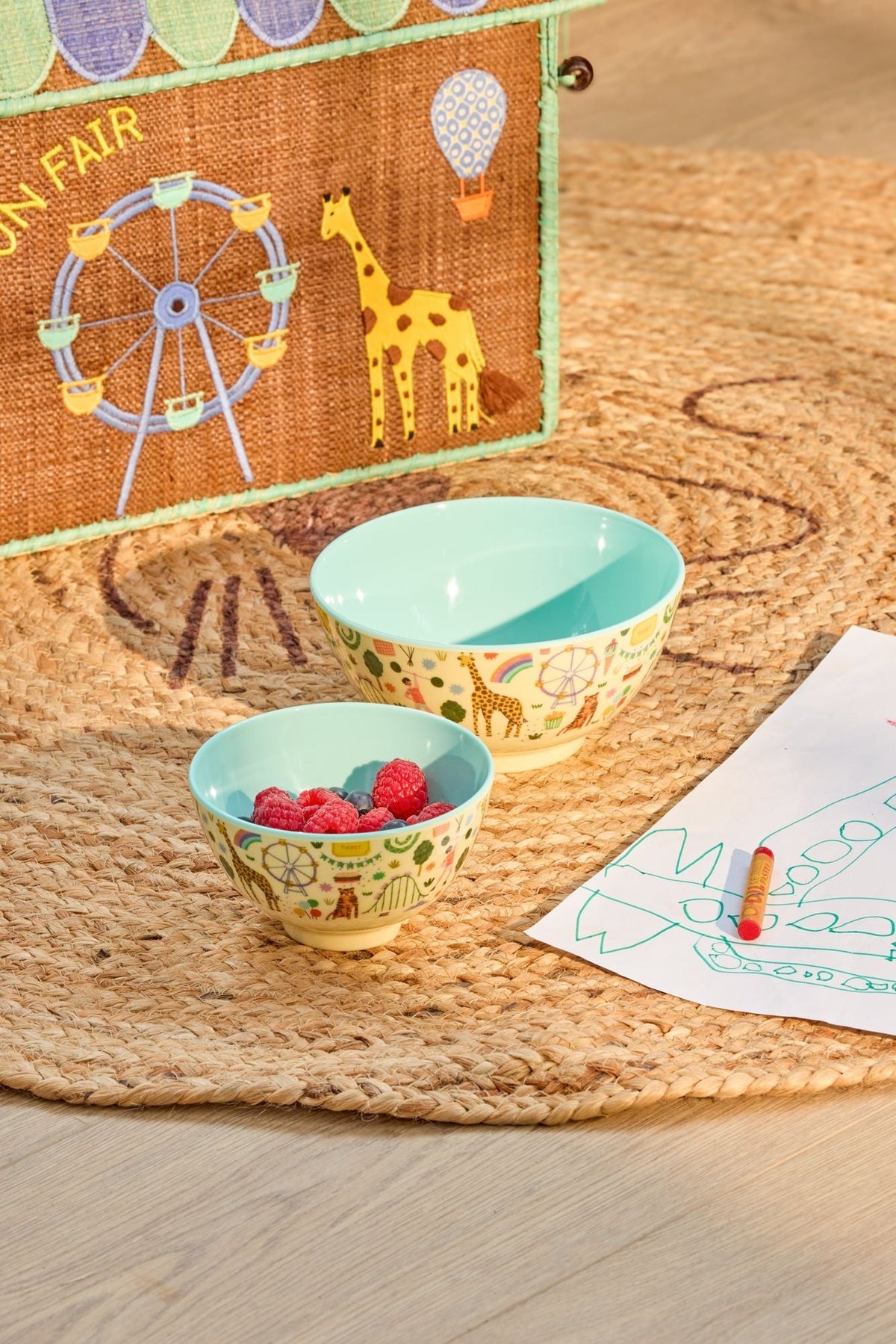 Kleine en grote kinderkom met kermisprint op een jute kleed, gevuld met frambozen
