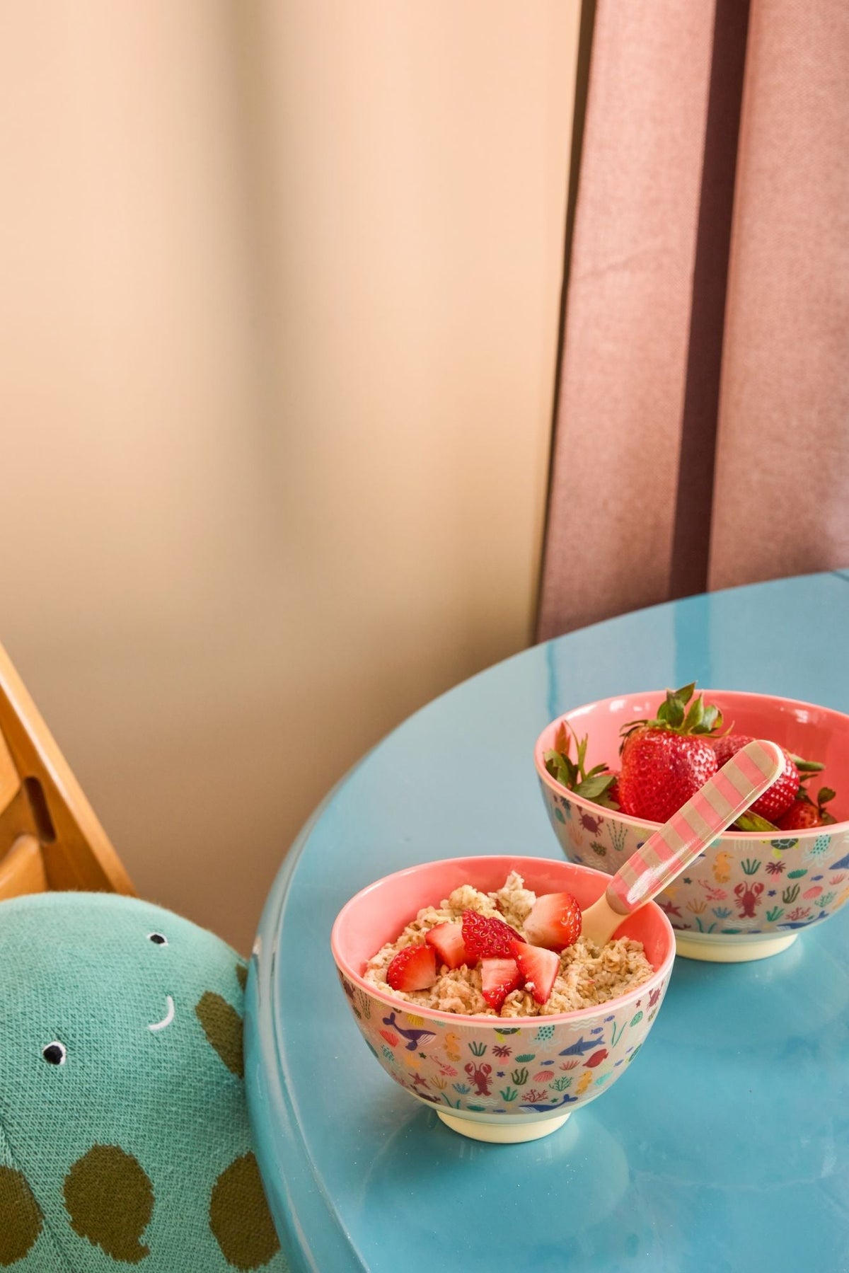 Twee kinderkommen met zeedierenprint gevuld met yoghurt en aardbeien op een blauw tafeltje