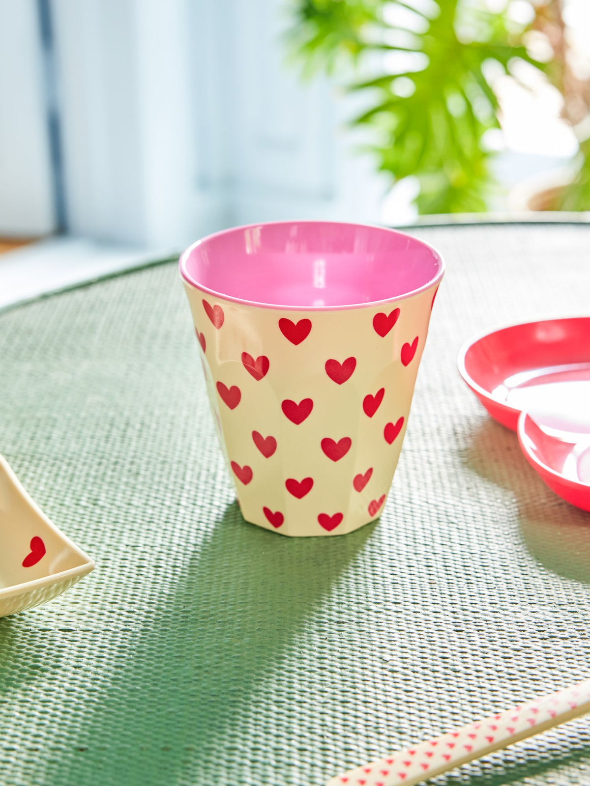 Melamine beker met hartjesprint op een tuintafel naast een roze schaaltje