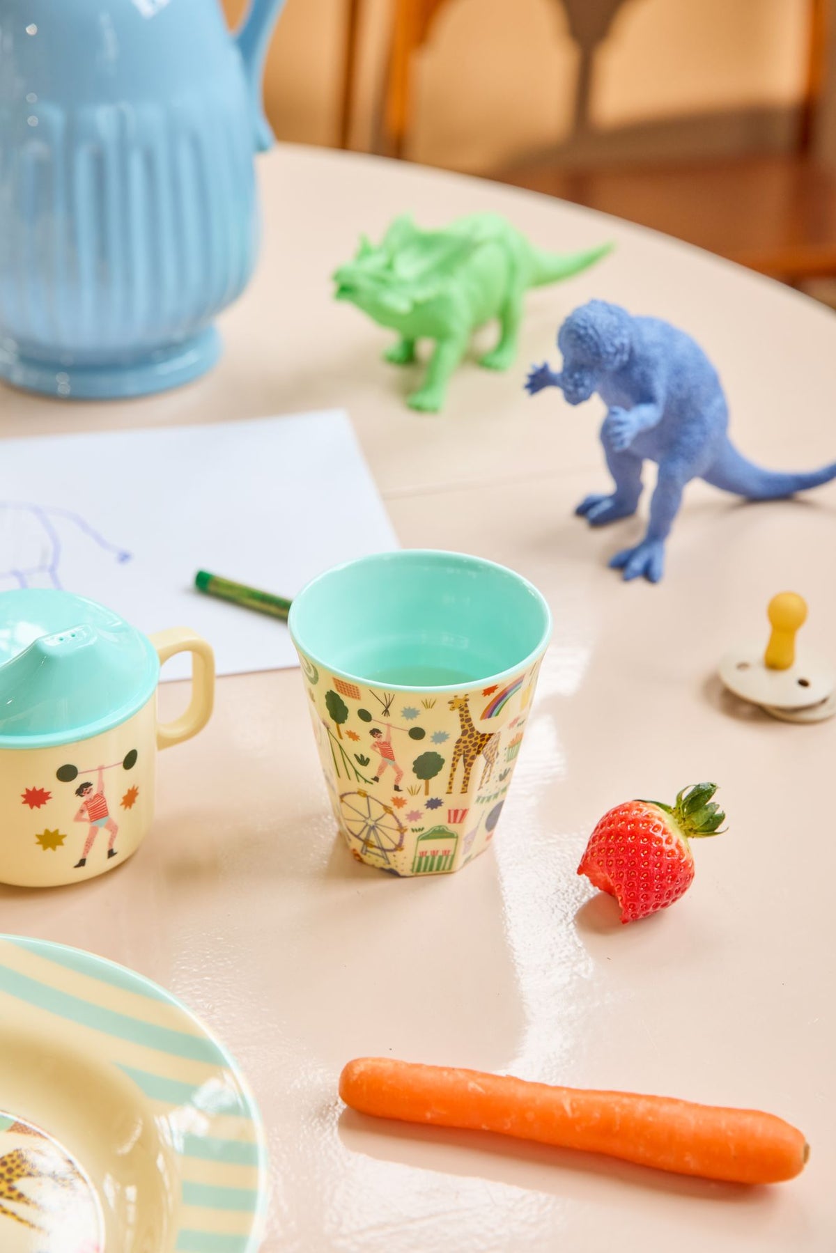 Kinderbeker met kermisprint op een tafel met speelgoeddino's, aardbei en wortel