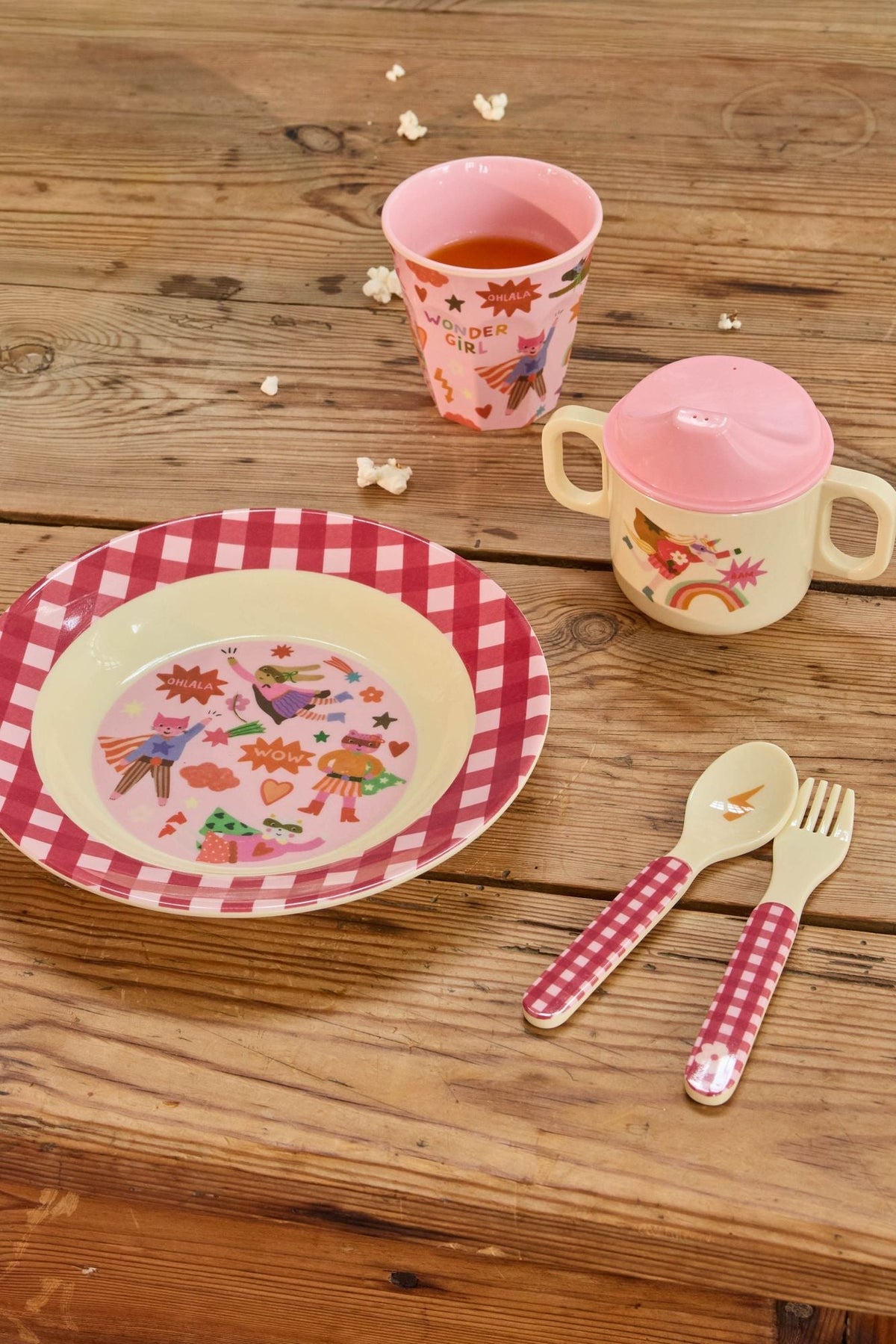 Roze kinderbeker met limonade naast een kinderbord en bestek op een houten tafel