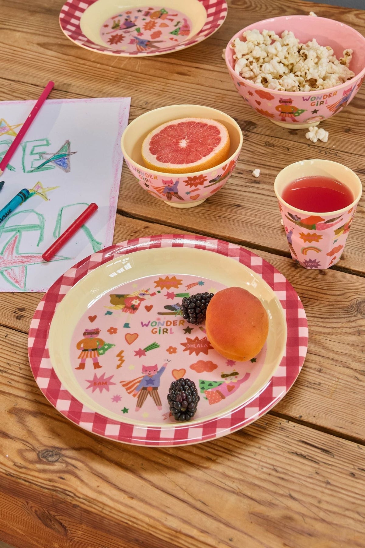 Roze kinderbeker, kom en bord met Wonder Girl-print op een houten tafel met fruit