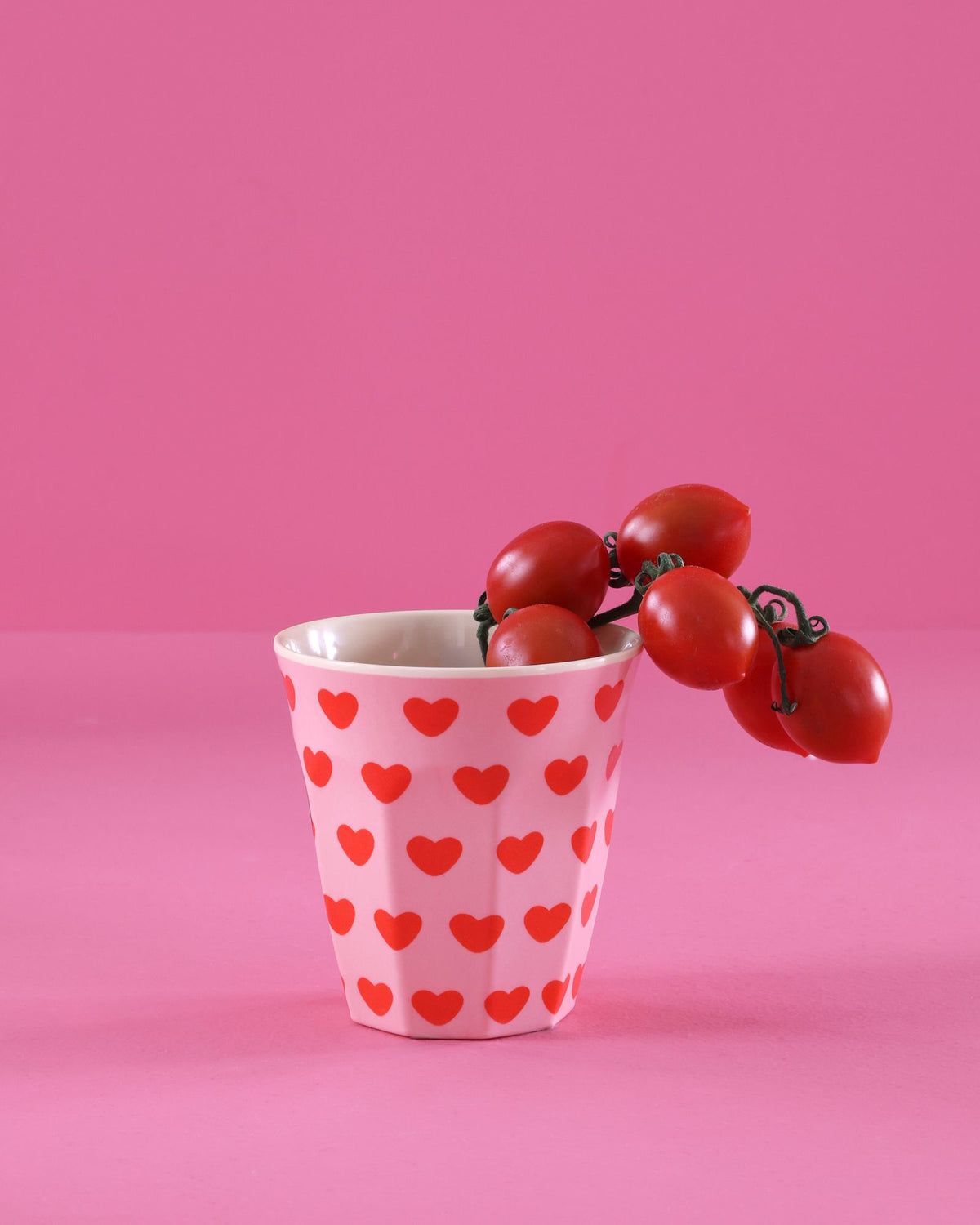 Roze melamine beker met hartjes en een trosje tomaten op een roze achtergrond