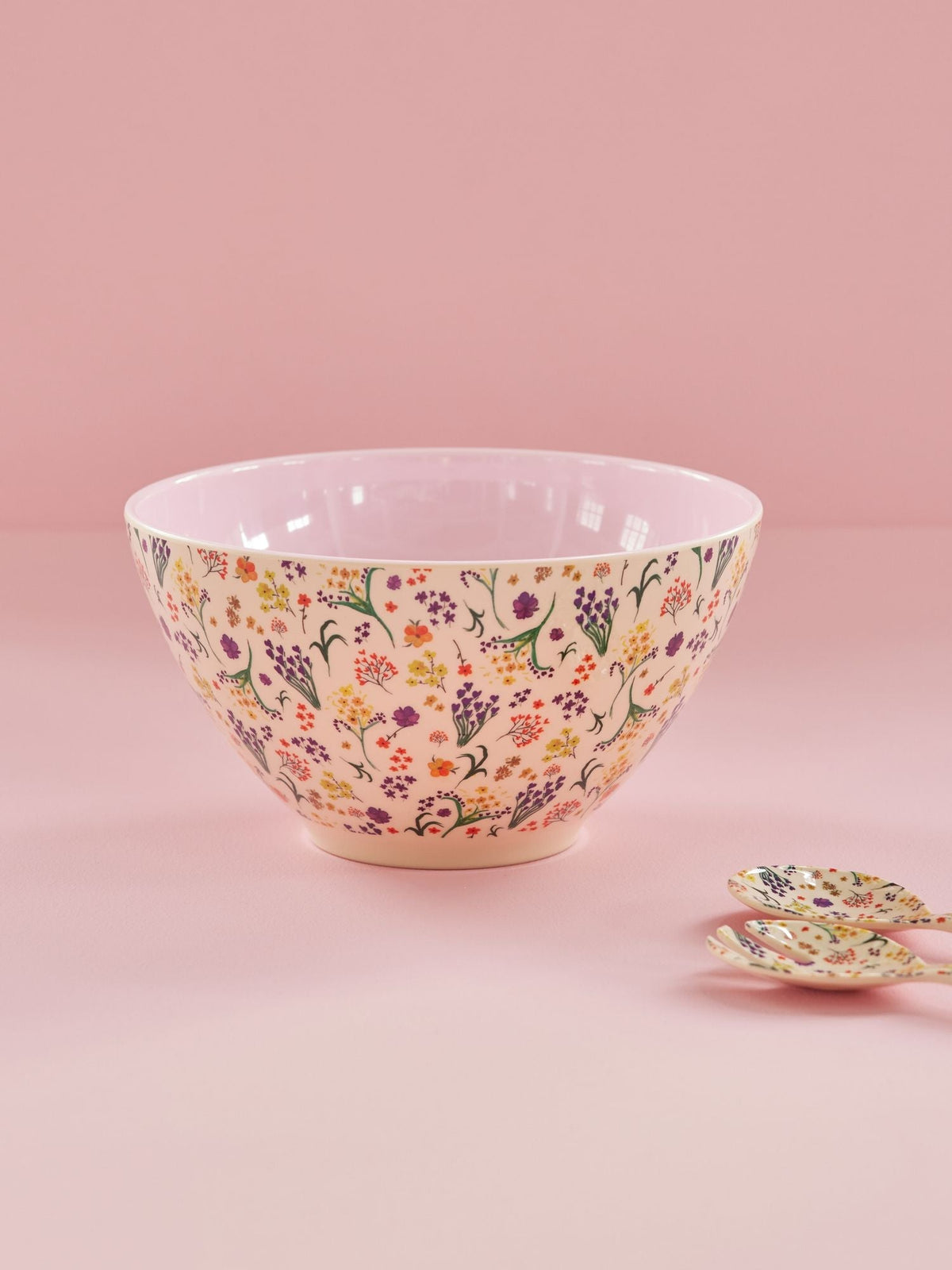 Saladeschaal met bloemenprint op een roze ondergrond naast twee saladelepels