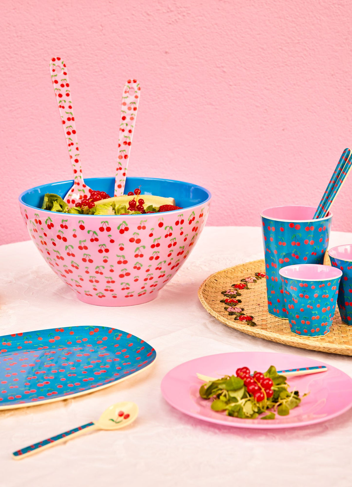Saladeschaal met salade en het roze saladebestek met kersenprint op een gedekte tafel