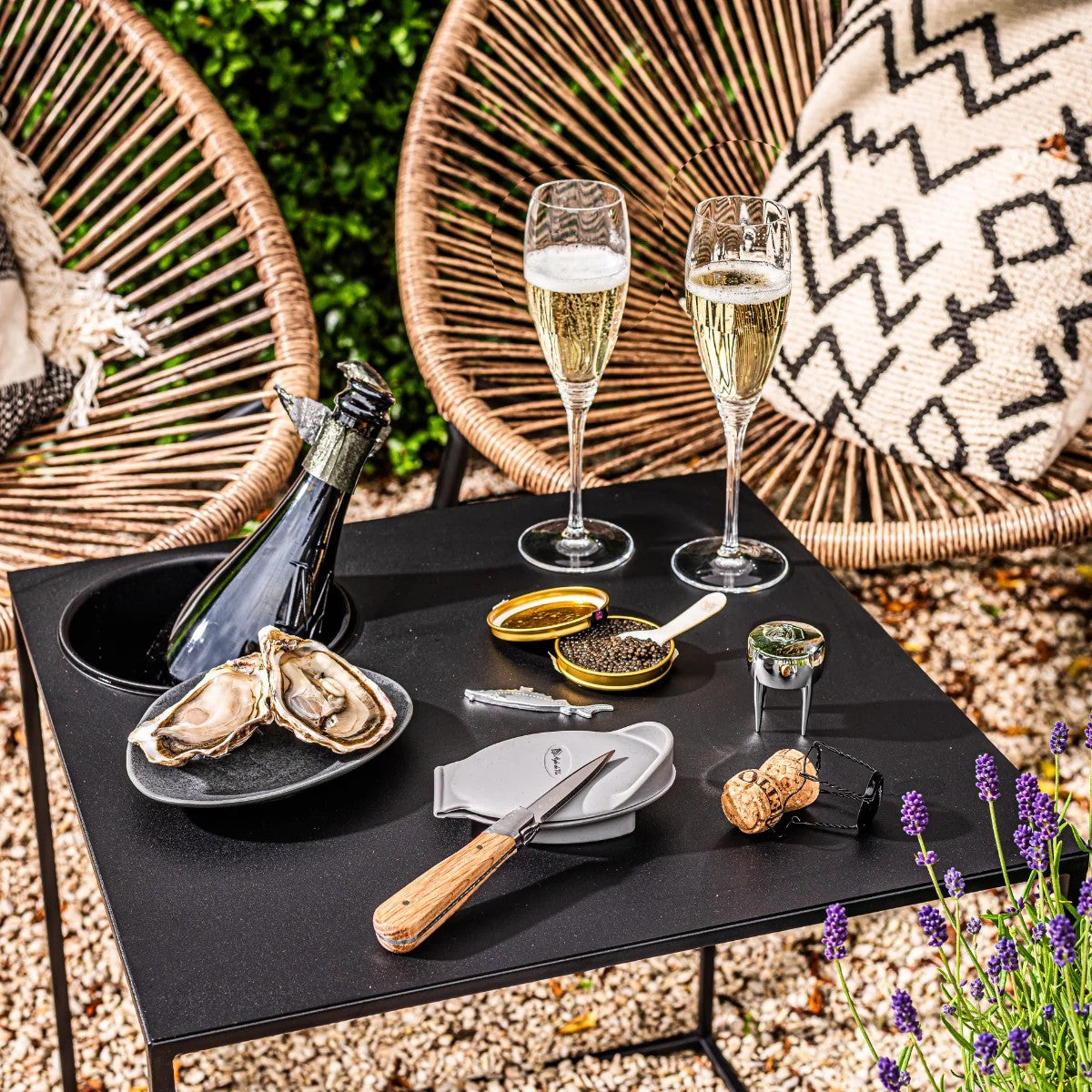 De set op een zwart tafeltje in de tuin, met oesters, kaviaar en glazen champagne
