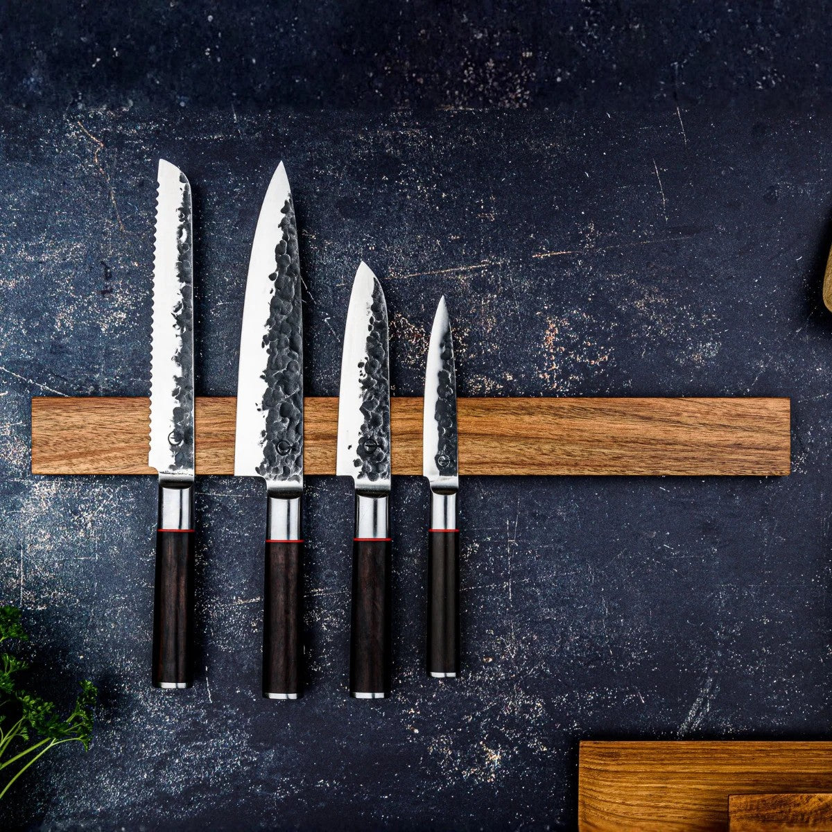 Het messenrek met een broodmes, een santoku en twee kleinere messen op een donkere ondergrond