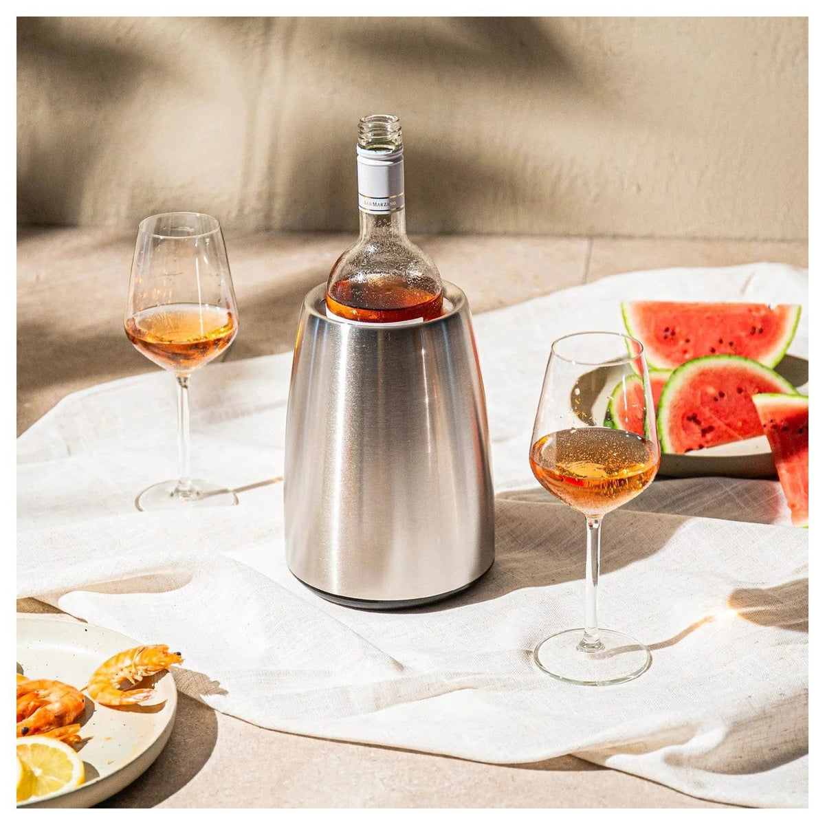 De roestvrijstalen Elegant wijnkoeler met fles op een gedekte tafel met watermeloen en glazen