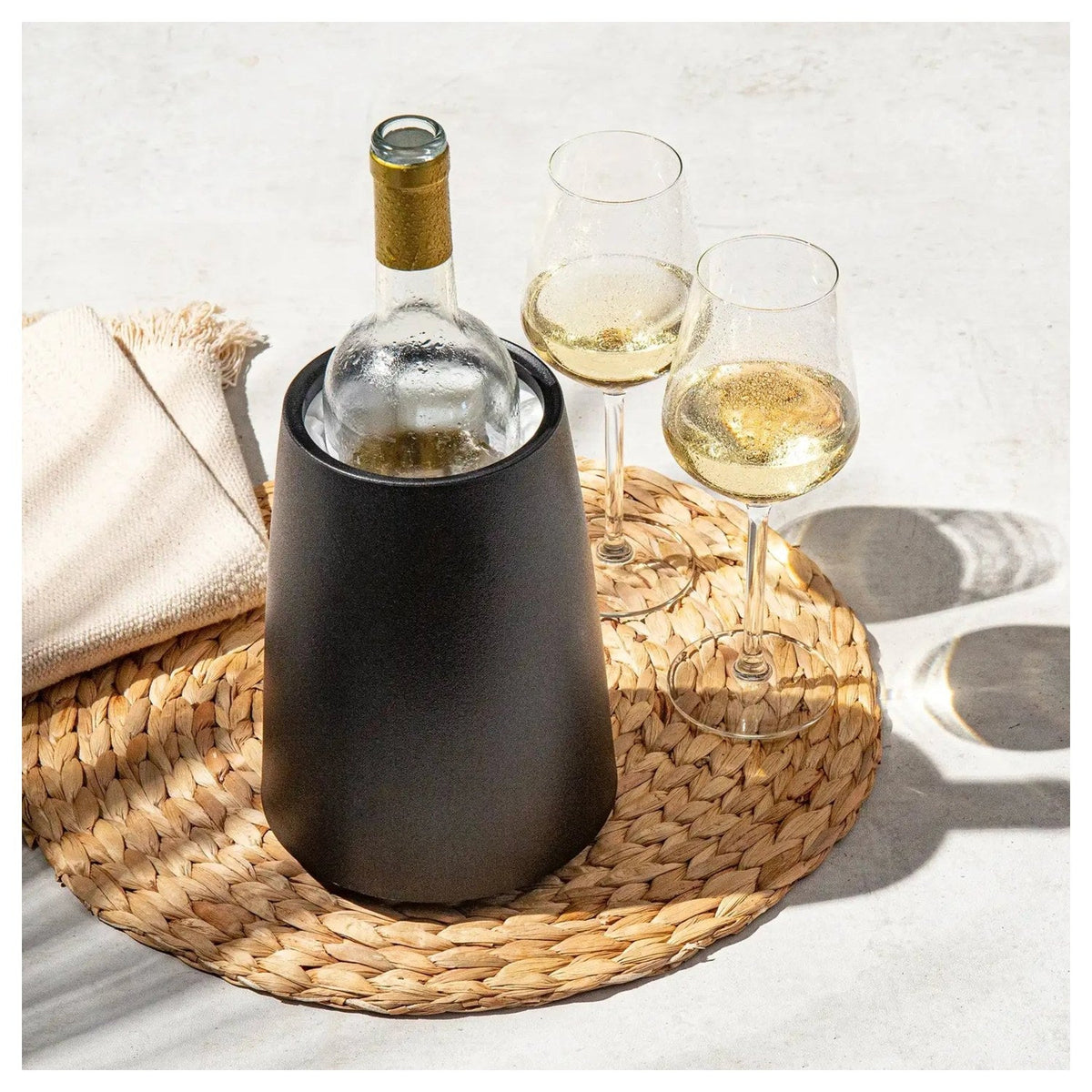 De zwarte Elegant wijnkoeler met fles op een rieten onderzetter met twee glazen