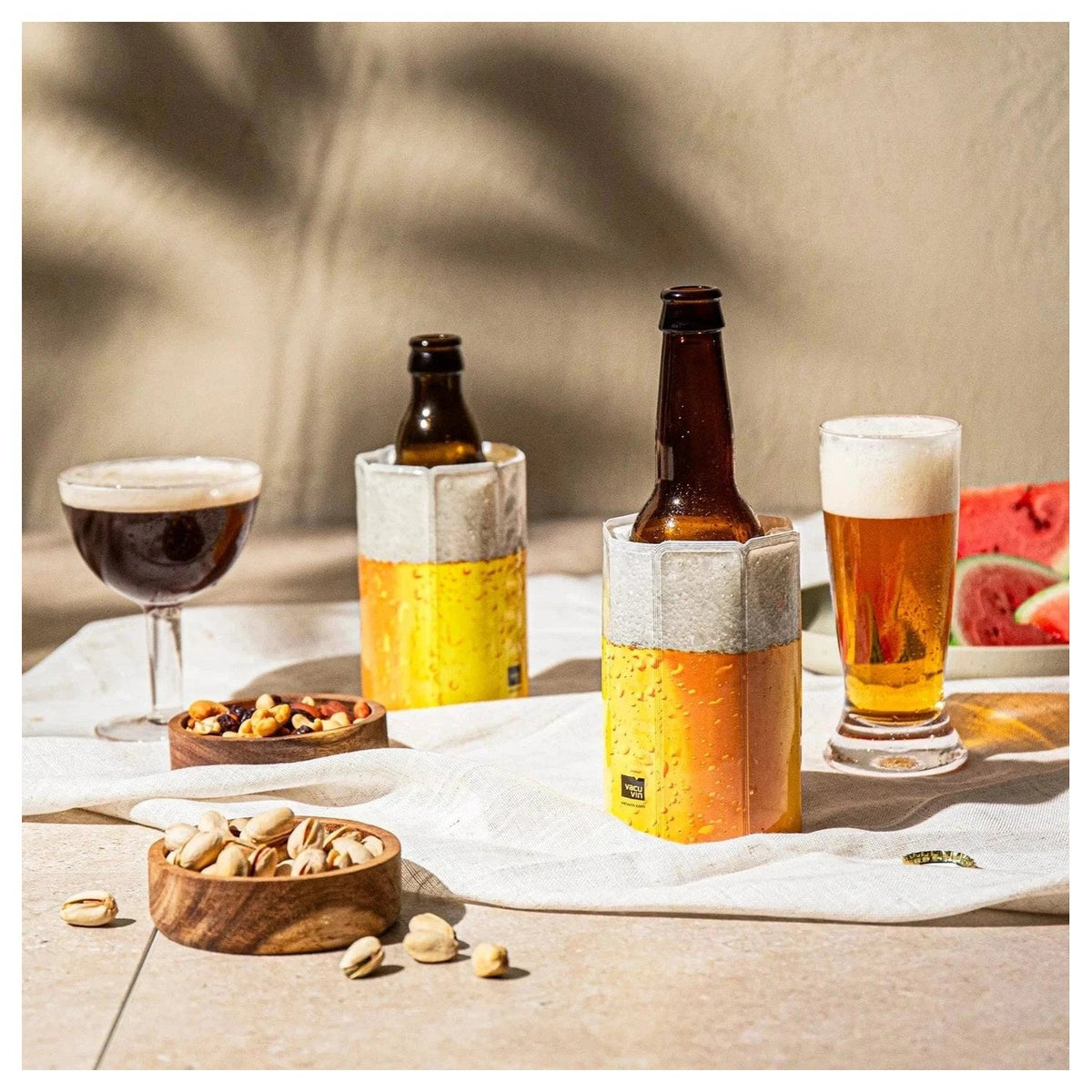 De koelhoes om een bierflesje naast een glas bier en nootjes