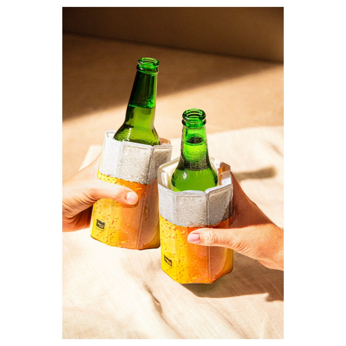 Twee handen houden twee bierflesjes met koelhoes vast