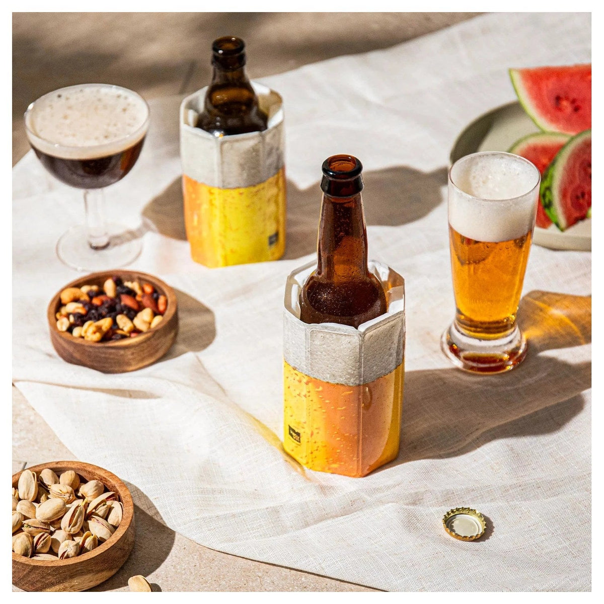 De koelhoes om een bierflesje op een gedekte tafel met glazen en nootjes