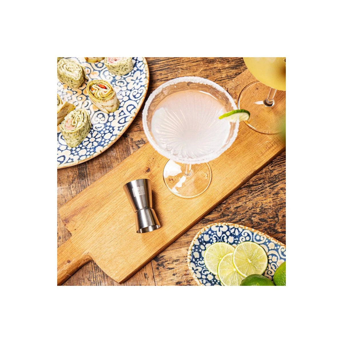 Het roestvrijstalen barmaatje op een houten plank naast limoenen en een cocktailglas