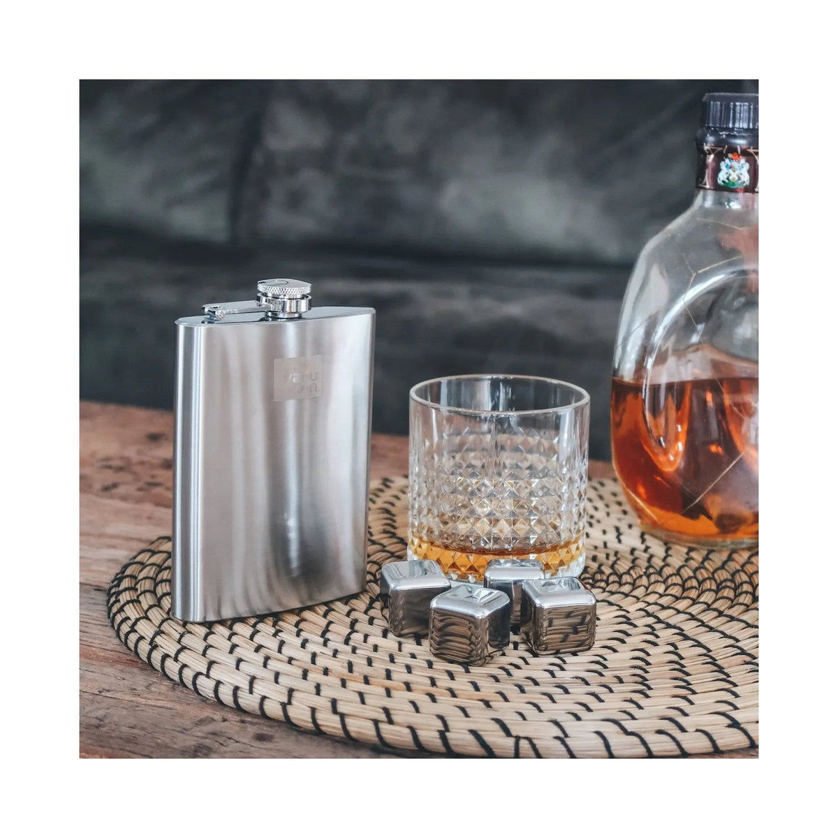 De heupfles op een houten tafel naast een glas whisky met ijsstenen