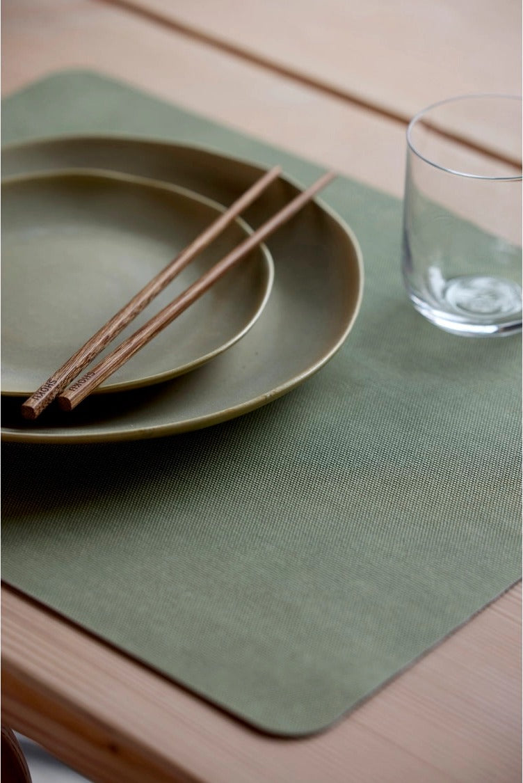 Shoku placemat Pure Green onder twee groene borden, een glas en houten eetstokjes op een houten tafel